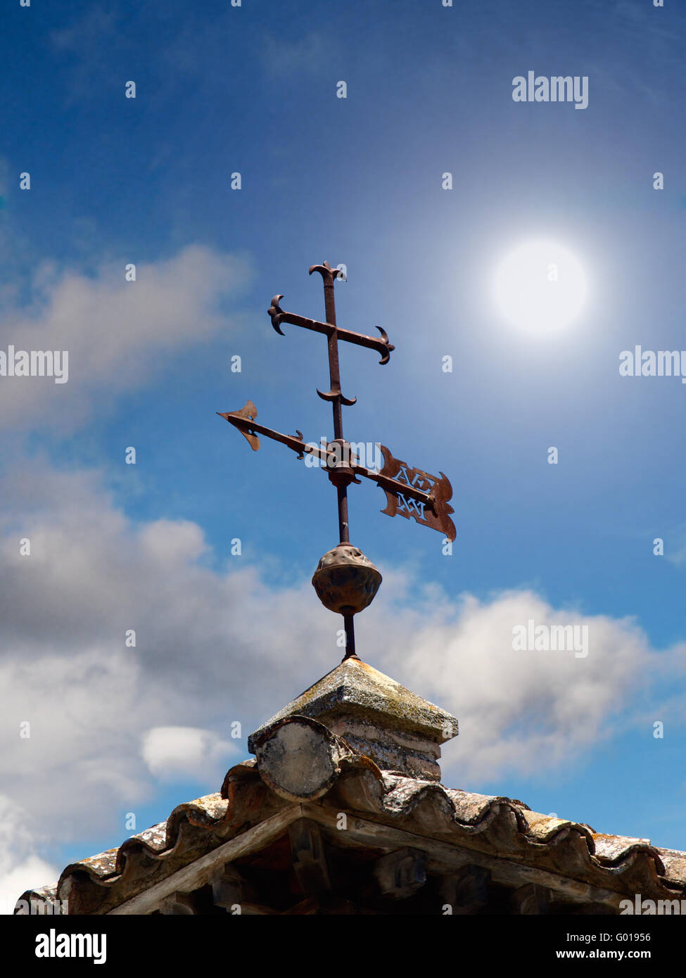 rostige Wetter Kreuz auf dem Dach einer alten Kirche mit bewölktem Himmel und Sonne Stockfoto