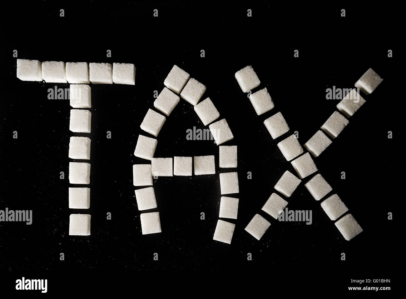 Wort Steuer machte der weißen raffinierten Zuckerwürfel auf schwarzem Schiefer Hintergrund symbolisiert Zucker Steuer Stockfoto