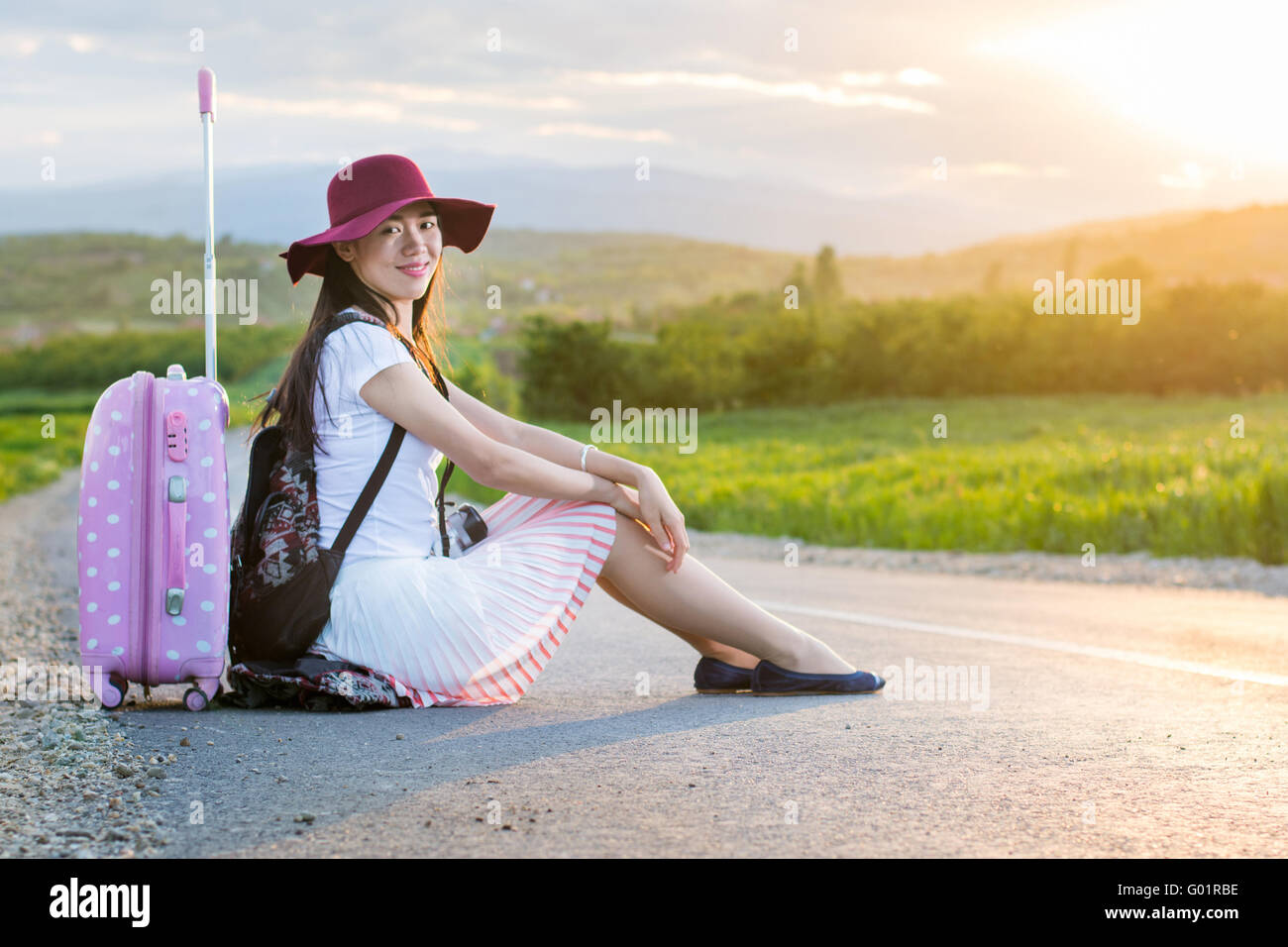 Einsames Mädchen sitzen auf der Straße neben dem Koffer Stockfoto