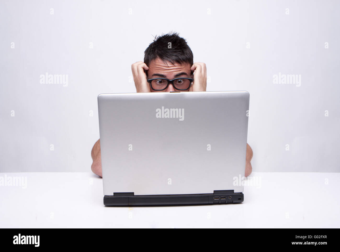 Ein Studioportrait von einem kaukasischen Mann verzweifelt auf der Suche. Isoliert auf weißem Hintergrund mit Brille arbeiten auf seinem laptop Stockfoto