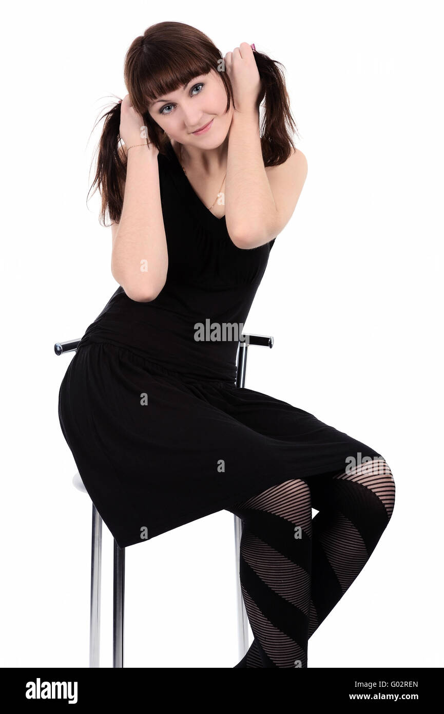 Mädchen im schwarzen Kleid sitzt auf einem hohen Stuhl, isoliert Stockfoto