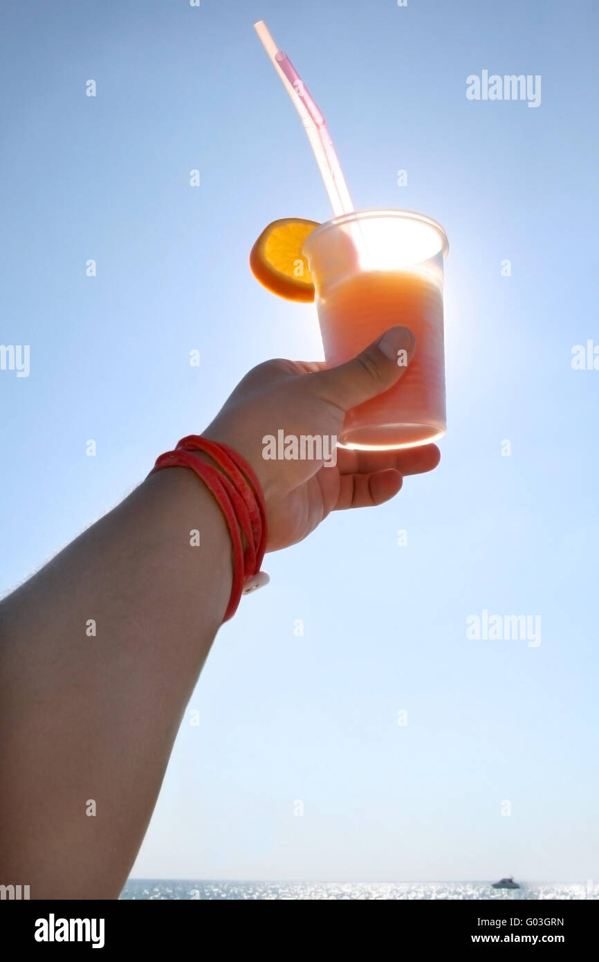 Hand, die eine cocktail Tequila Sunrise auf dem Hintergrund des Meeres mit Luxus-Yacht am Horizont Stockfoto