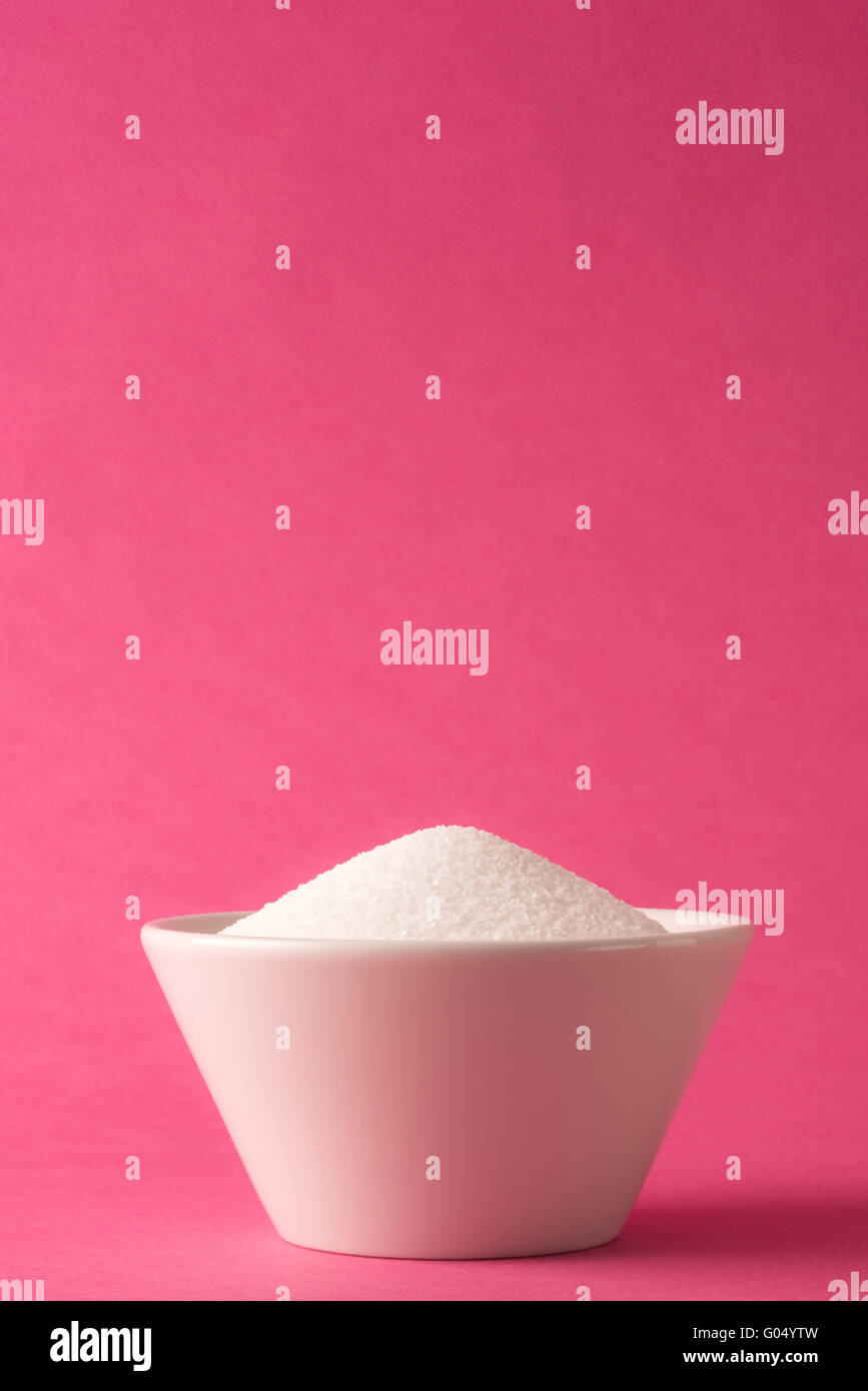 Weiße Schale voll von weißem Zucker vor rosa Hintergrund Stockfoto