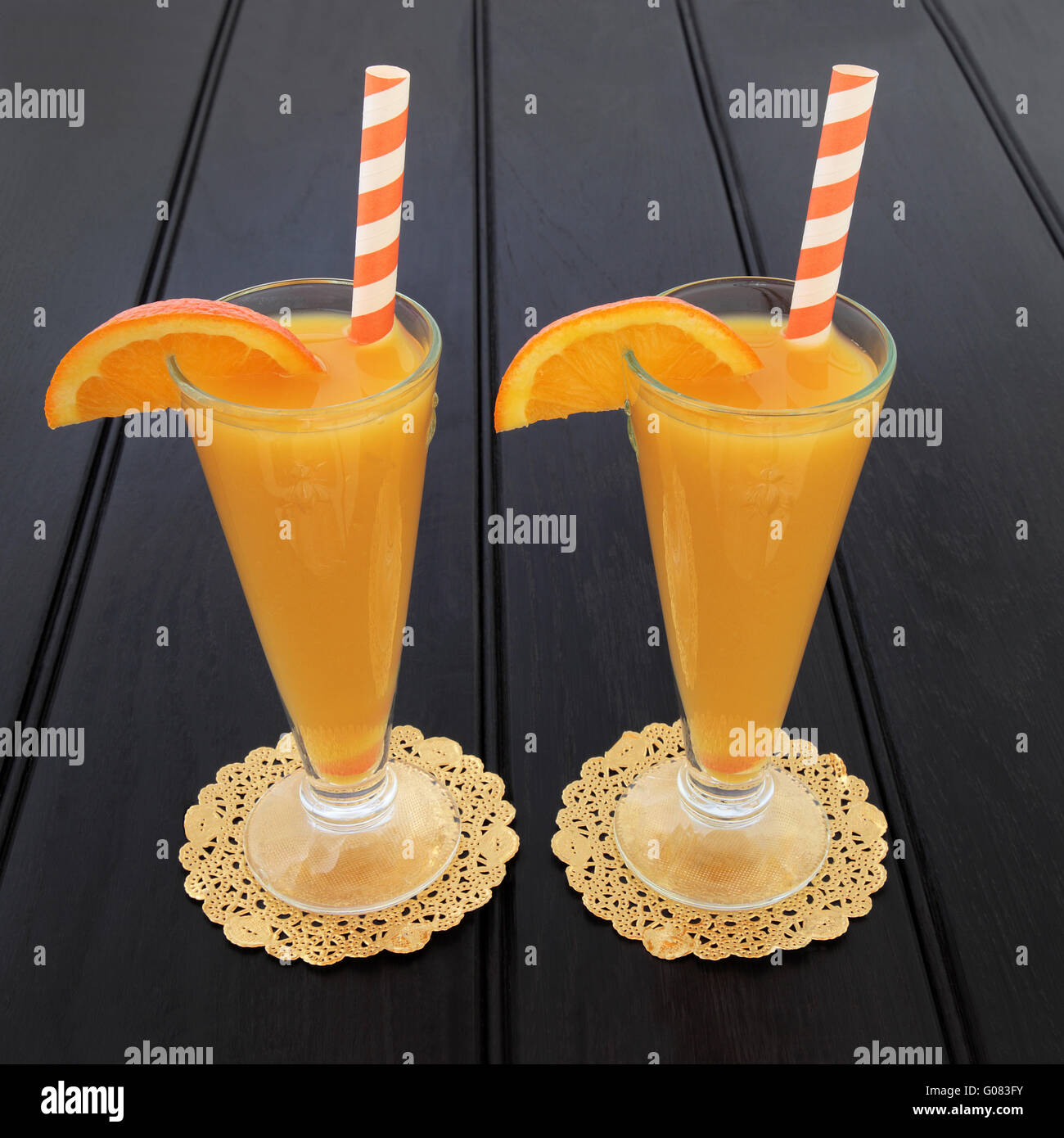 Orange Fruchtsaft Trinken in Gläsern auf gold Deckchen mit gestreiften Strohhalme in dunklem Holz. Stockfoto