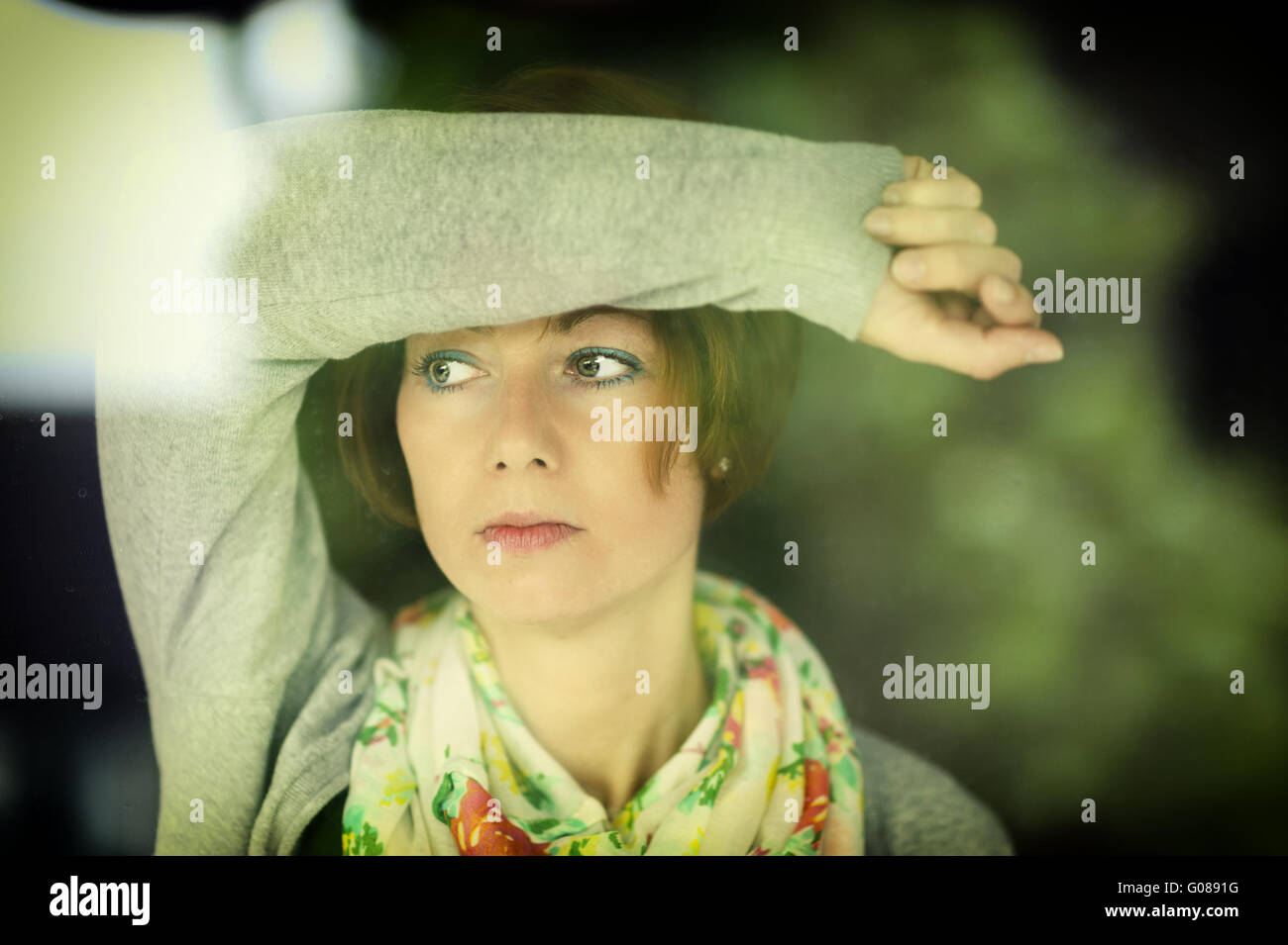 junge Frau, die nachdenklich durch ein Fenster Stockfoto
