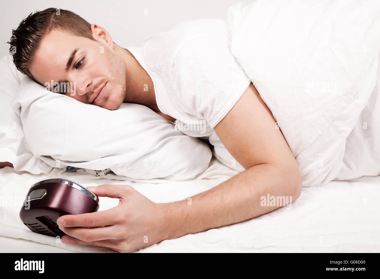 schöner junger Mann im Bett Blick auf Uhr Stockfoto