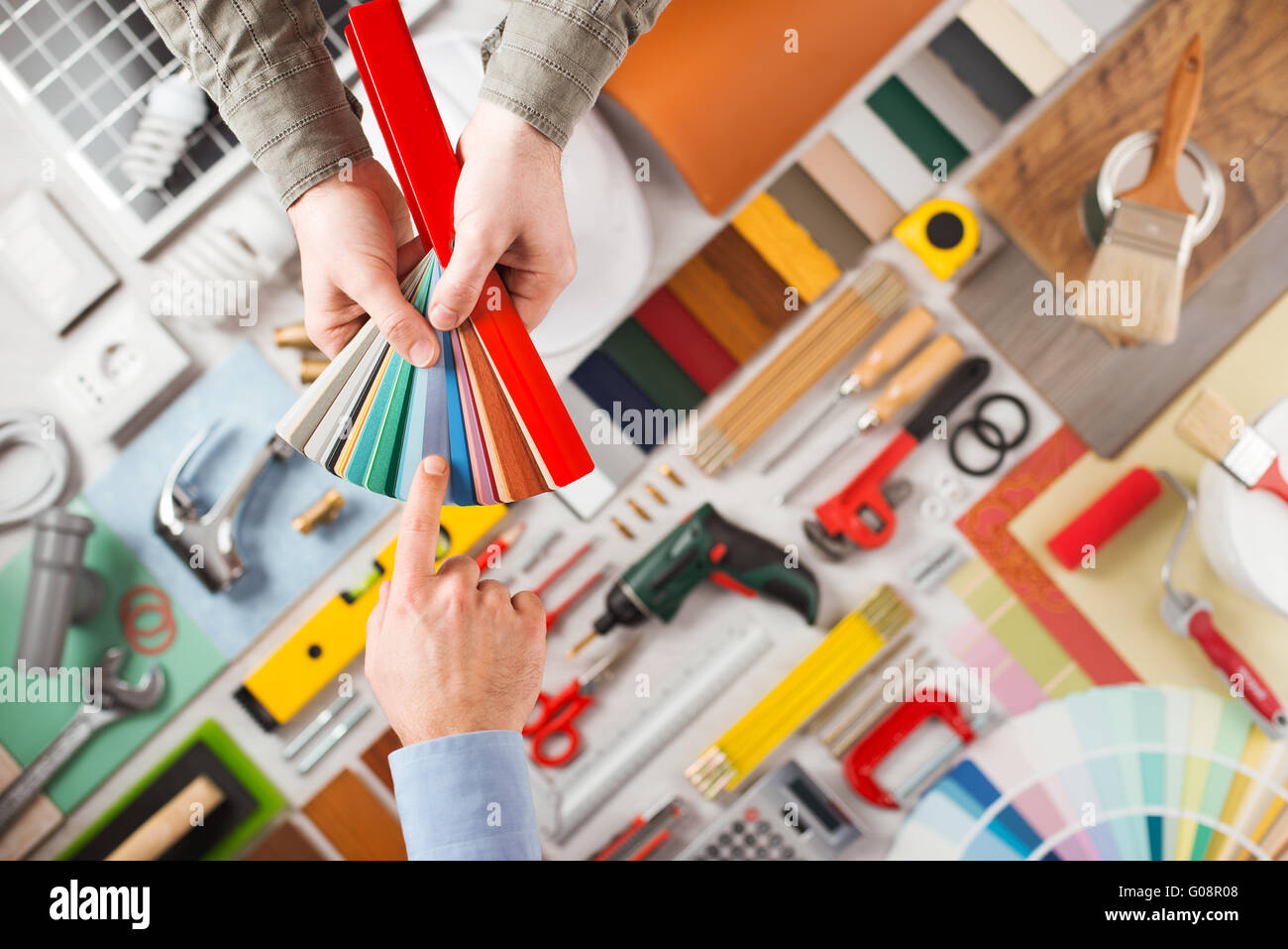 Männliche Hände halten Farbfelder und Wahl der richtigen Farbe, Arbeitsmittel auf Hintergrund Draufsicht, DIY und Renovierungs-Konzept Stockfoto