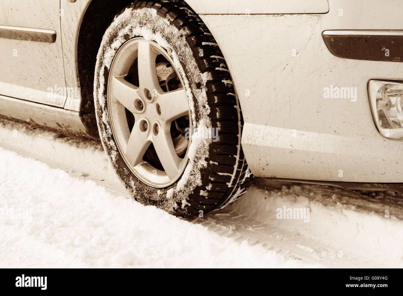 Nahaufnahme von Pkw-Reifen auf einer verschneiten Straße - Sepia-Farbton Stockfoto