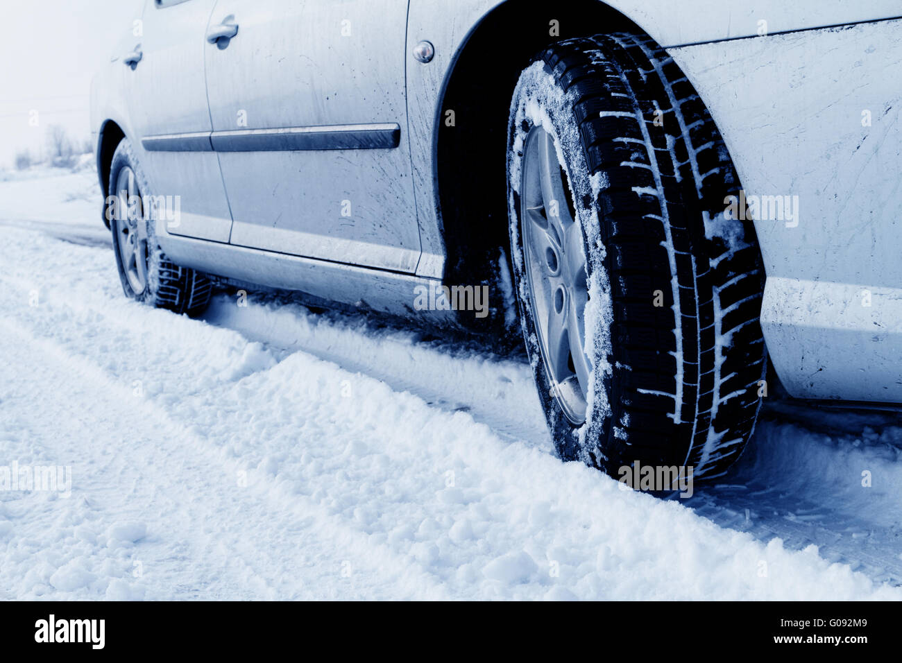 Nahaufnahme von Pkw-Reifen auf einer verschneiten Straße - Blauton Stockfoto