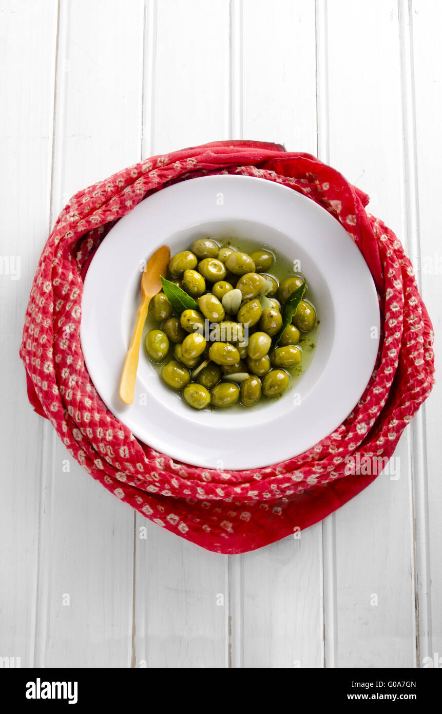 Eine weiße Schale gefüllt mit grünem Knoblauch marinierte Oliven, eingehüllt in einen roten Schal auf weißem Hintergrund Stockfoto