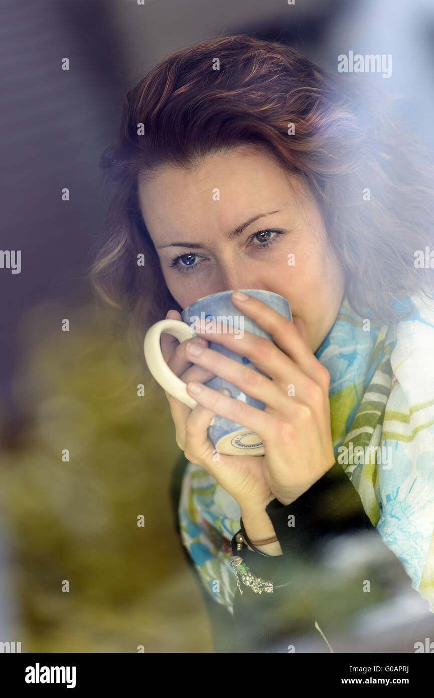 junge Frau mit einer Tasse Tee hinter dem Fenster Stockfoto