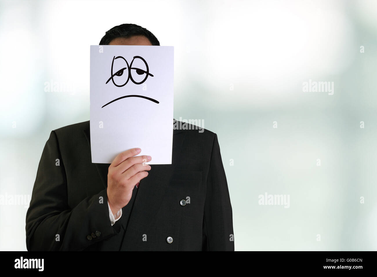 Firmen-Konzept-Image eines Geschäftsmannes Weißbuch Maske mit traurig und müde Gesicht drauf halten Stockfoto
