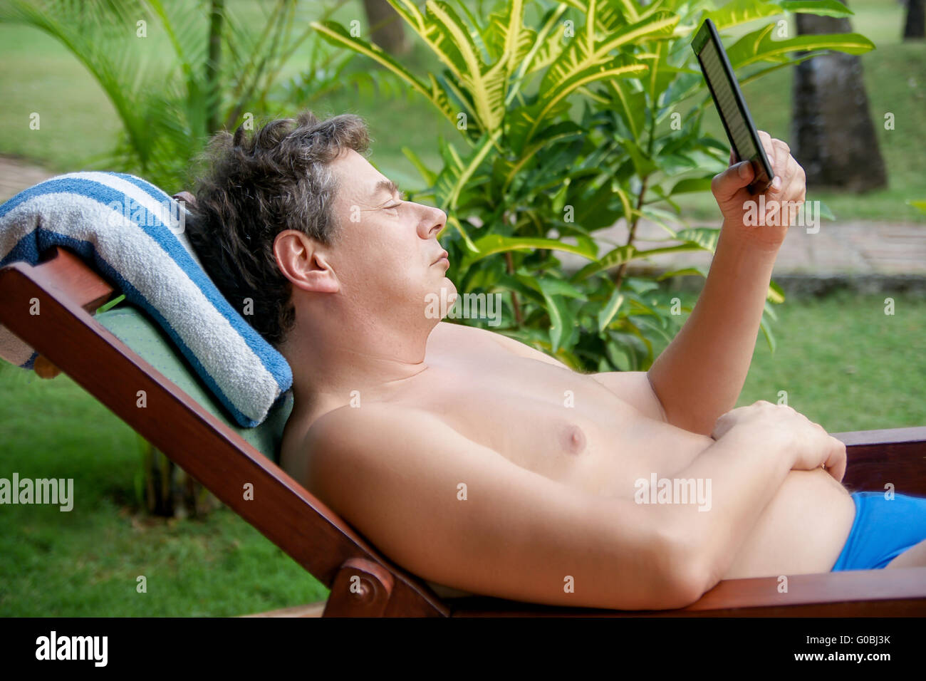 Mann in einem Liegestuhl ist in ein E-Book-Reade lesen. Stockfoto
