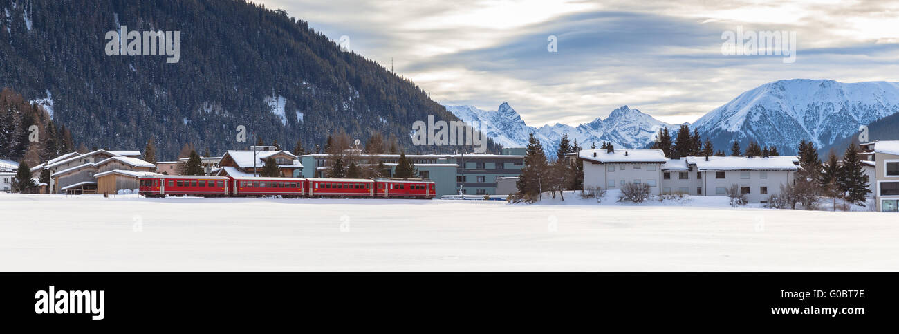 Roter Zug durch Davos Dorf im Winter mit Schnee bedeckt Alpen im Hintergrund Stockfoto