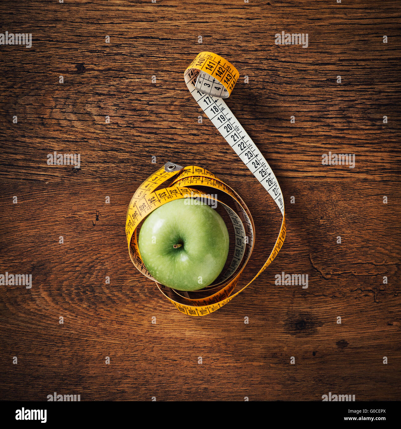 Grüner Apfel, eingewickelt in ein Maßband auf einem Holztisch, Draufsicht, Ernährung und Gewicht-Verlust-Konzept Stockfoto
