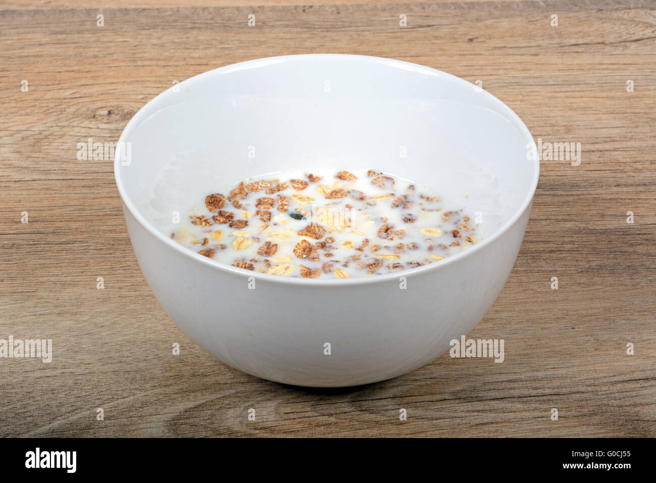 Müsli mit einer Mischung aus gesunden Früchten, Nüssen und Samen und Milch in einer Schale gegen eine hölzerne Hintergrund, England, UK. Stockfoto