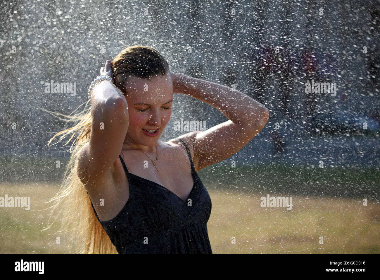 Junge Frau nimmt eine Erfrischung unter einem sprinkler Stockfoto