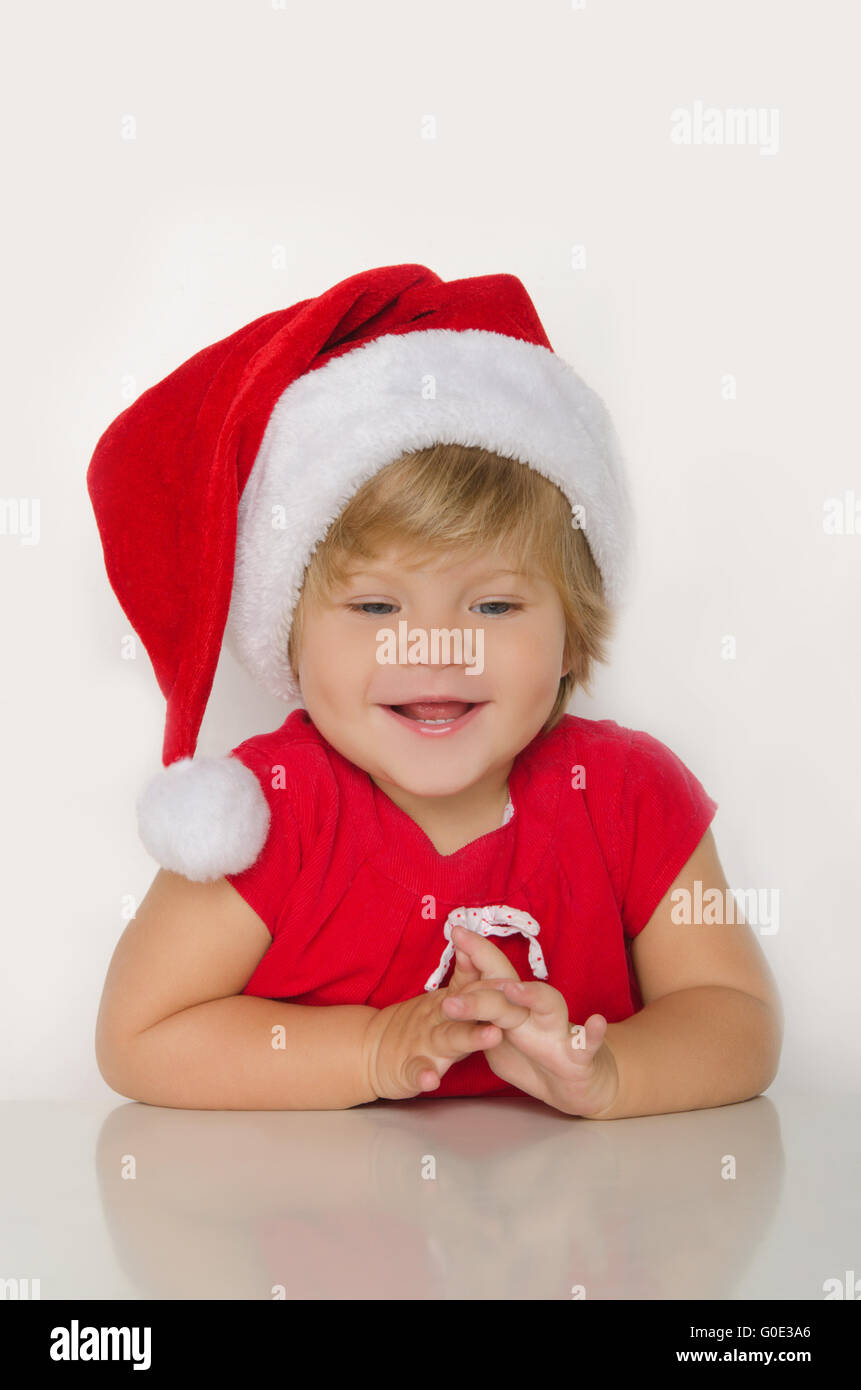 Mädchen im Kostüm des Weihnachtsmanns am Tisch und lächelt Stockfoto