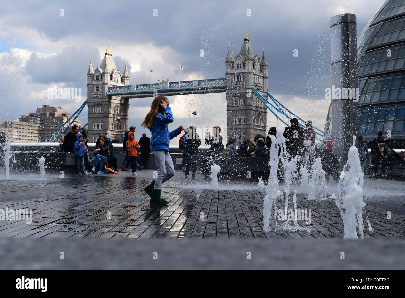 Kinder spielen in ein Wasserspiel am More London Tower Bridge und ein bewölkter Himmel im Hintergrund. Stockfoto