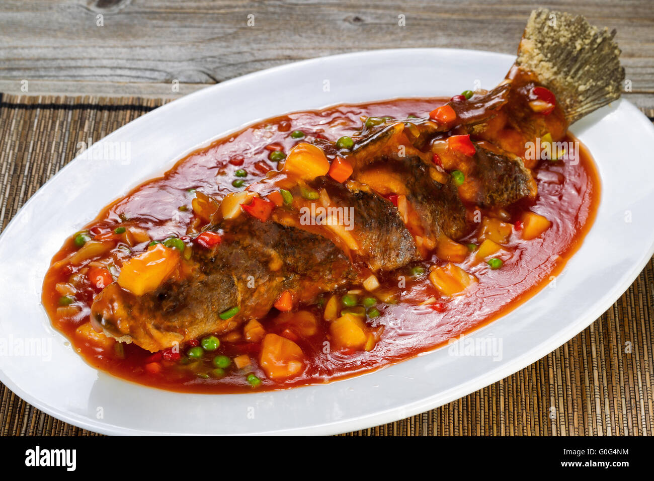 Gebratener ganzer Fisch in Sauce mit Obst und Gemüse in weiß Teller bereit, Essen Stockfoto