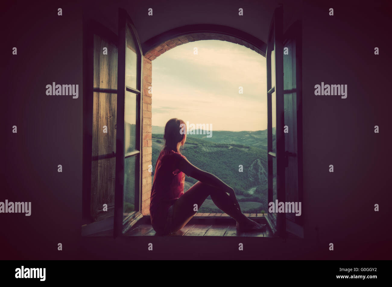 Junge Frau sitzt in einem geöffneten alten Fenster Blick auf die Landschaft der Toskana, Italien. Stockfoto