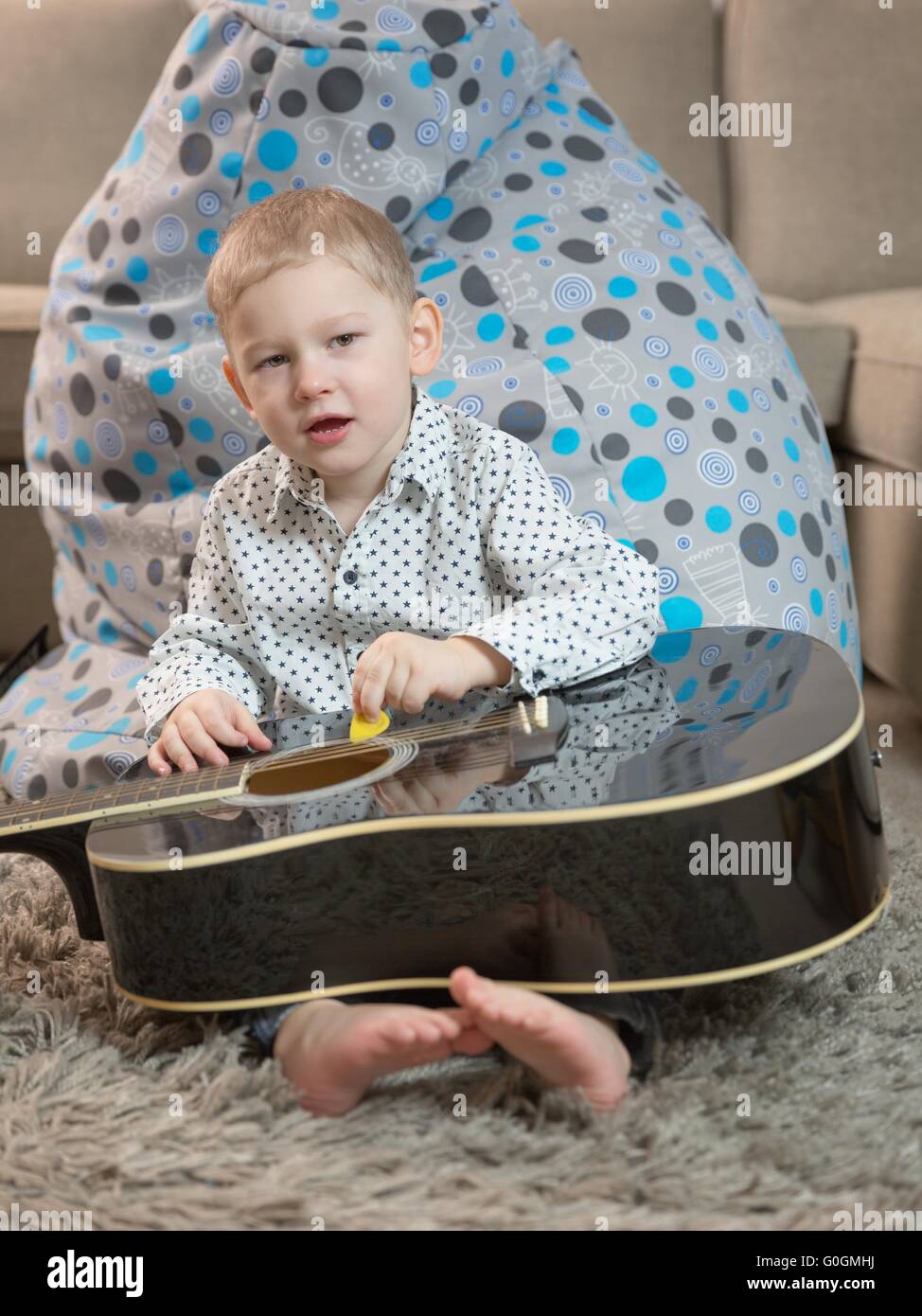 Wenig fröhlicher Junge spielt die Gitarre hits Stockfoto