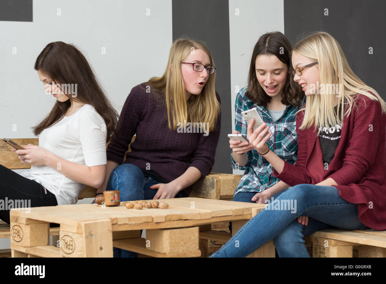 Teenager-Gruppe unterhält sich mit Handys und zeigt verschiedene Gesichtsausdrücke Stockfoto
