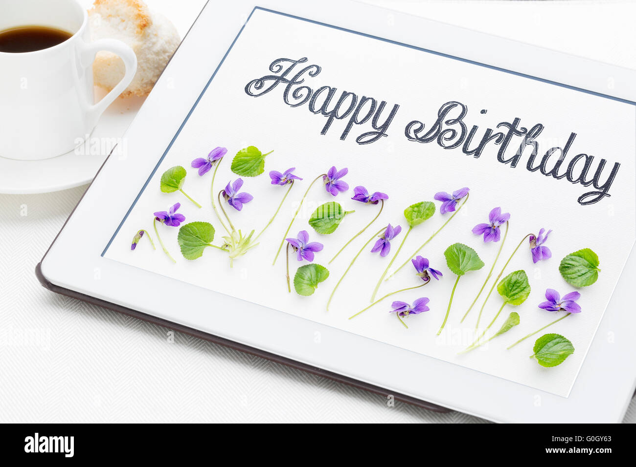 Glücklich Geburtstag Grußkarte - Handschrift mit Viola Blumen und Blätter auf digital-Tablette mit einer Tasse Kaffee Stockfoto