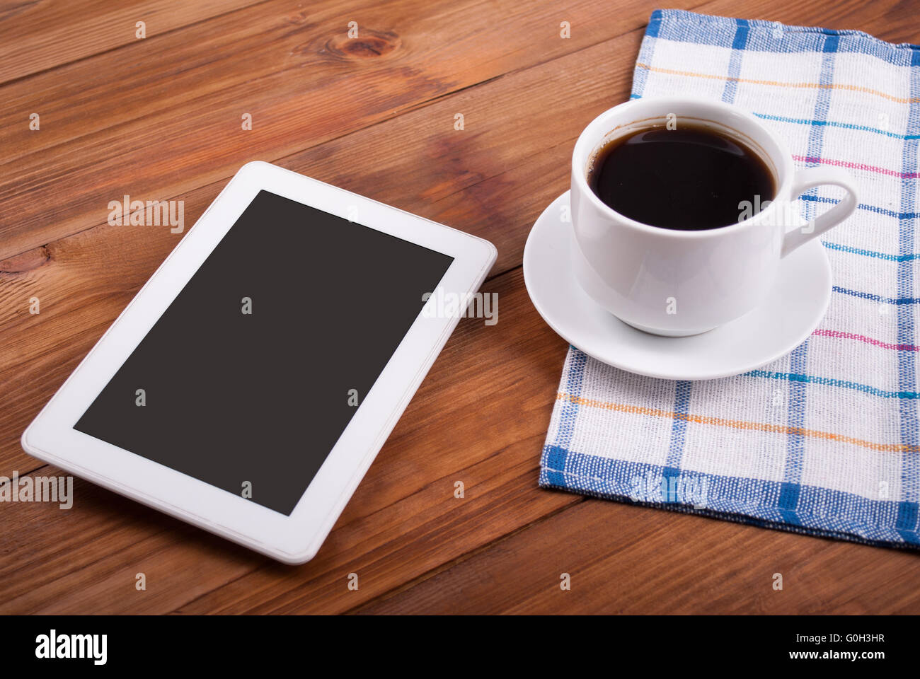 Digital-Tablette und Kaffeetasse auf einem Holztisch. Stockfoto