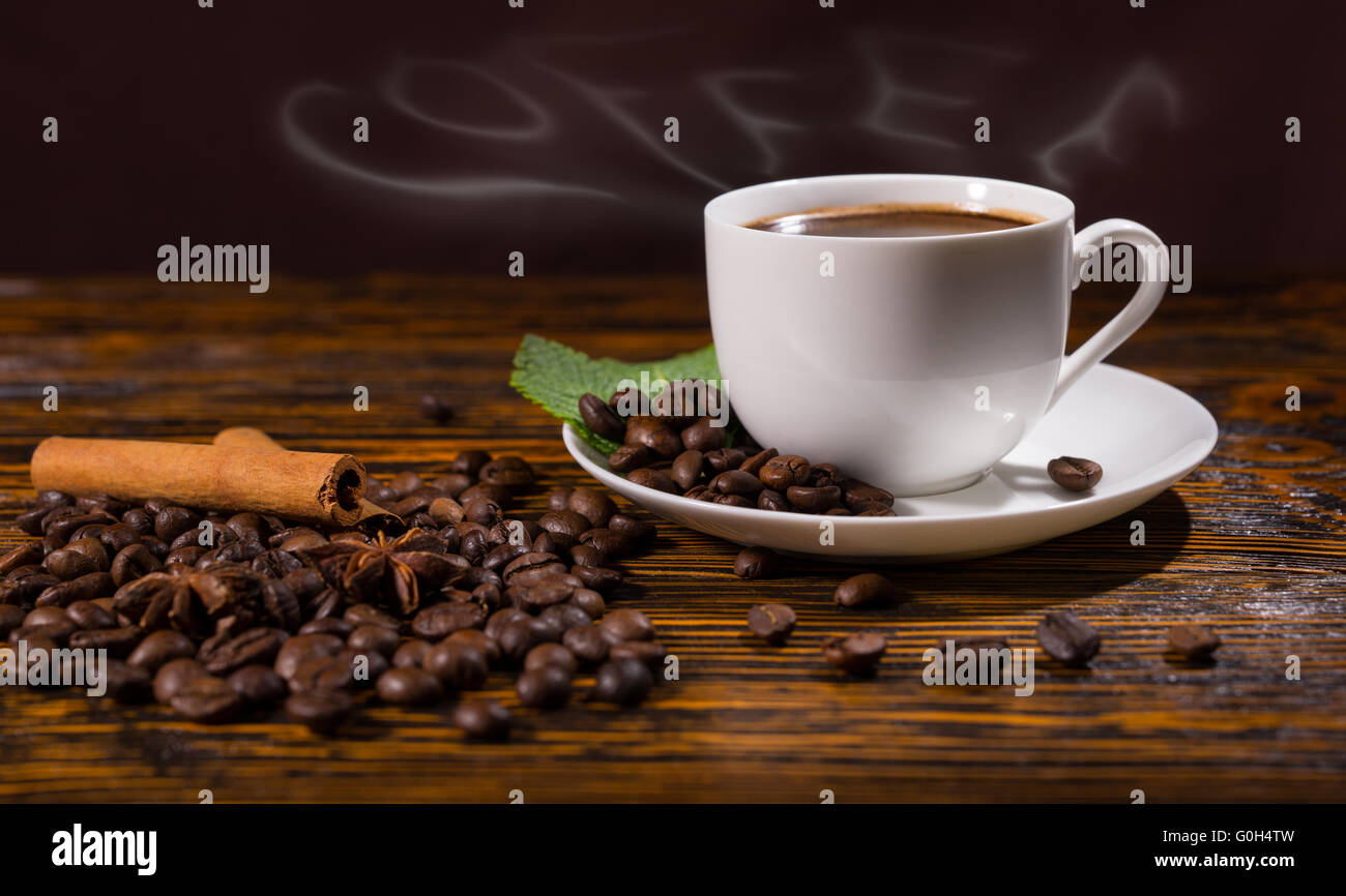 Dampfend heiße Tasse Kaffee mit Bohnen ausgebreitet, Untertasse und auf Holztisch Stockfoto