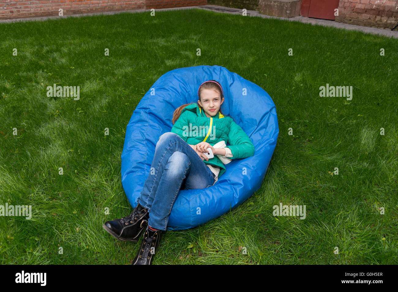 Junges Mädchen zum Entspannen in eine blaue Sitzsack auf einem üppig grünen Garten Rasen nach oben auf die Kamera ruhig lächelnd, mit Textfreiraum Stockfoto