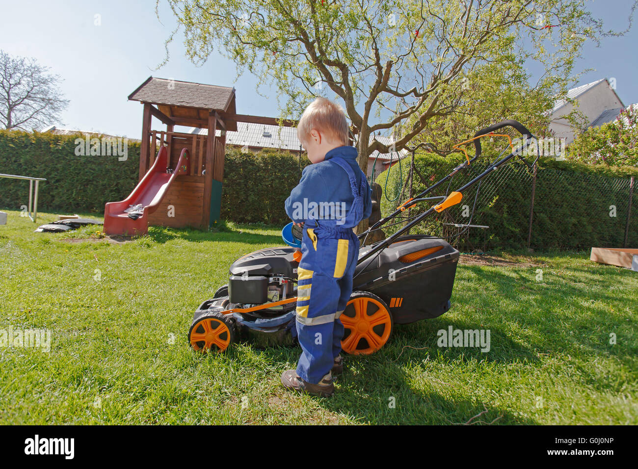 Süßen, kleinen Jungen mäht den Rasen. Junge inspiziert den Mäher vor treibende oder links Motoröl. Stockfoto