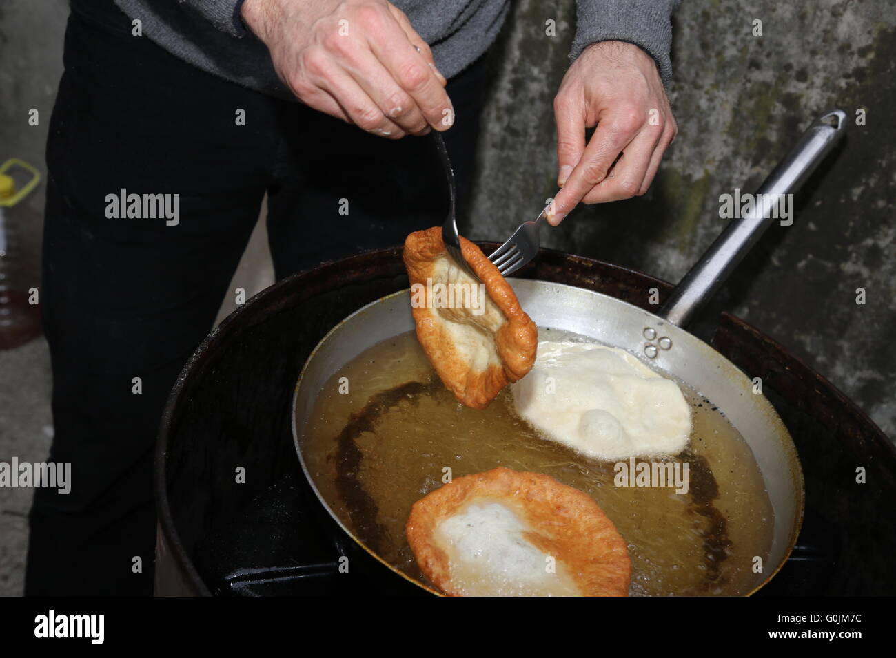 Hände zu kochen, während die große frittierten Krapfen Kochen eingetaucht in siedendem Öl in einen Aluminium-Topf Stockfoto