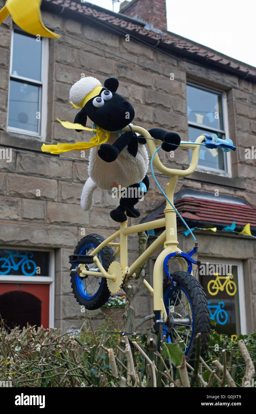Great Ayton, North Yorkshire UK, 1. Mai 2016. Viele Eigenschaften im Dorf sind zu Ehren des Radsport Tour de Yorkshire, dekoriert Etappe 3 von denen heute durch das Dorf führt. Unter dieser Adresse, auf die Tour-Route ist ein schrulliger Modell von Shaun das Schaf ein fröhlich eingerichteten thront in einem Garten Hecke Fahrrad. Stockfoto