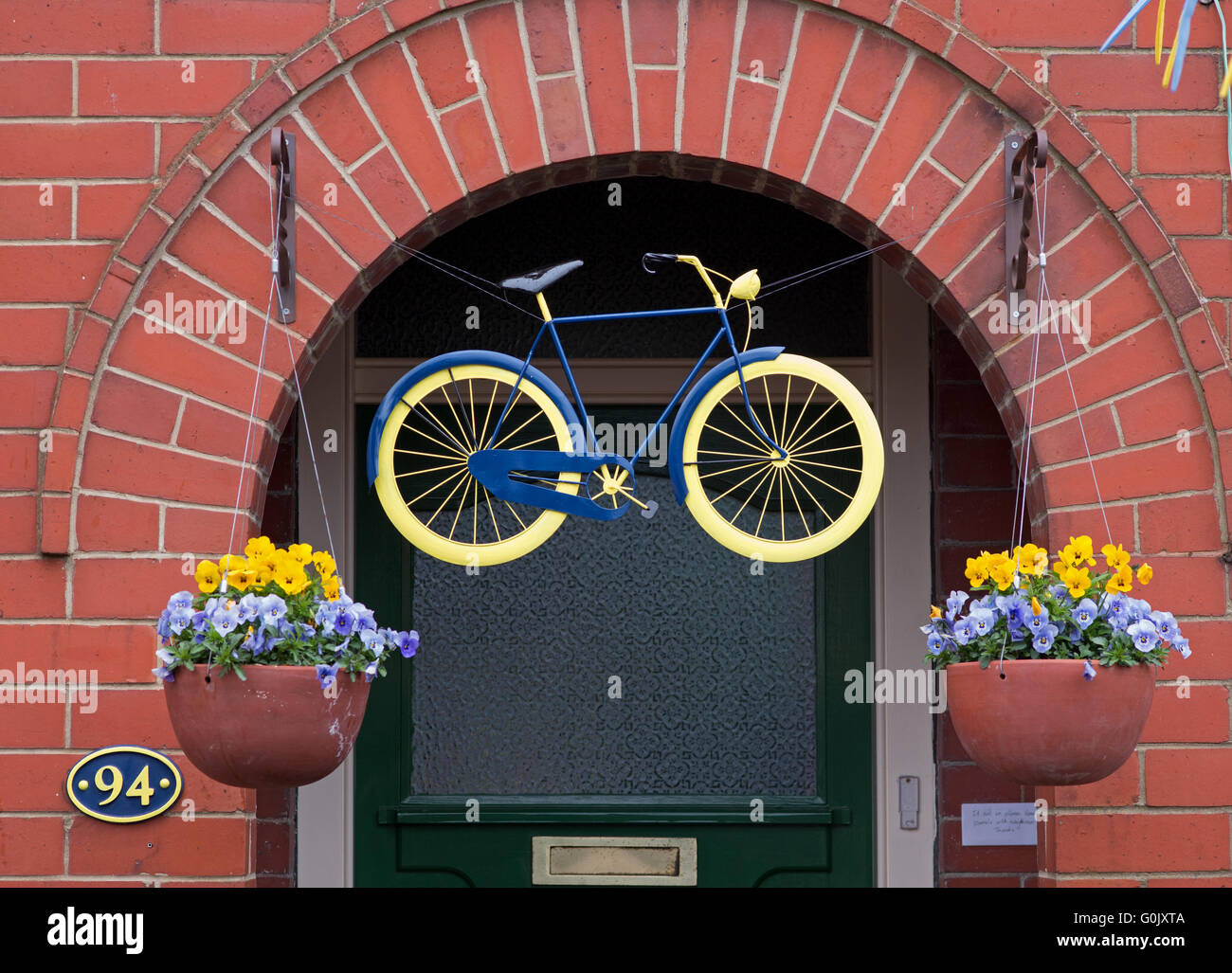 Great Ayton, North Yorkshire UK, 1. Mai 2016. Viele Eigenschaften im Dorf sind zu Ehren des Radsport Tour de Yorkshire, dekoriert Etappe 3 von denen heute durch das Dorf führt. Unter dieser Adresse hängt eine lackierte Rad über der Haustür, mit Blumen geschmückten Blumenampeln in den offiziellen Yorkshire Farben auf beiden Seiten. Stockfoto