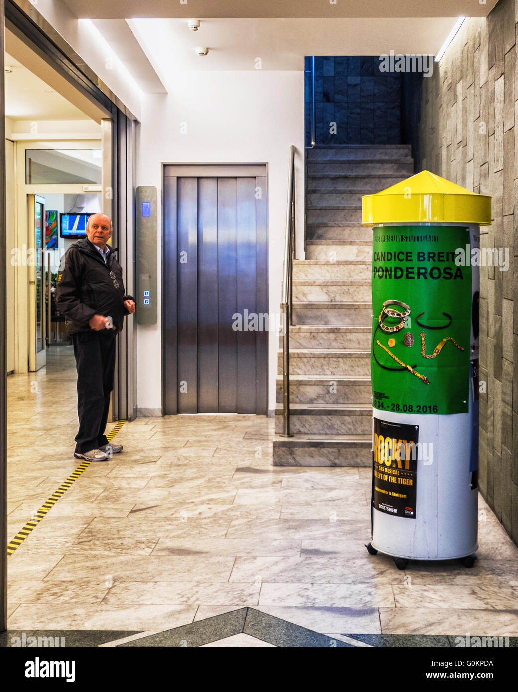 Stuttgart, Deutschland. Älterer Mann im gespiegelten Foyer Hotel Unger und Plakat für Künstler, Candice Breitz Kunstausstellung Stockfoto