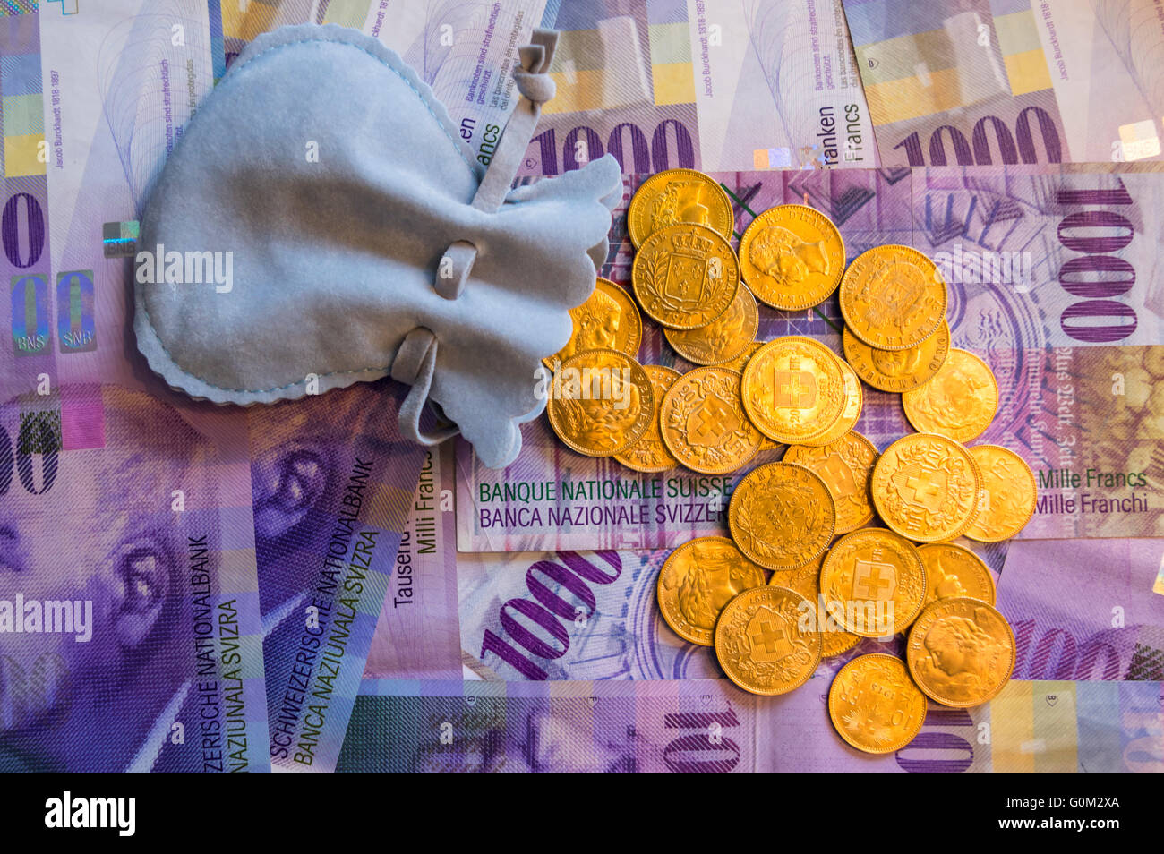 Viele 20 Franken gold Münzen gegossen aus einem kleinen Geldbeutel auf 1000 Schweizer Franken Banknoten. Stockfoto