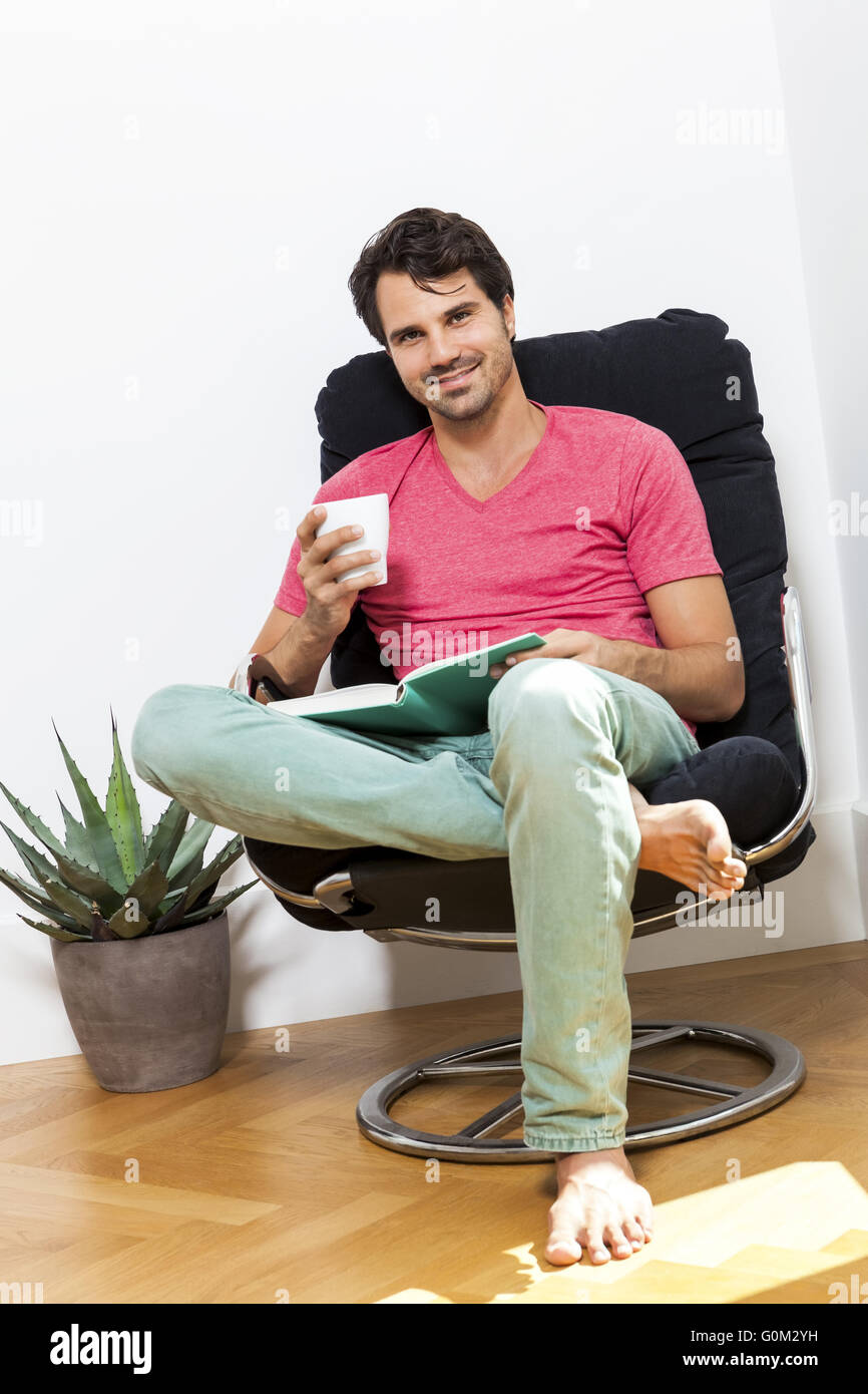 Mann auf Stuhl sitzend mit Buch und einem Getränk Stockfoto