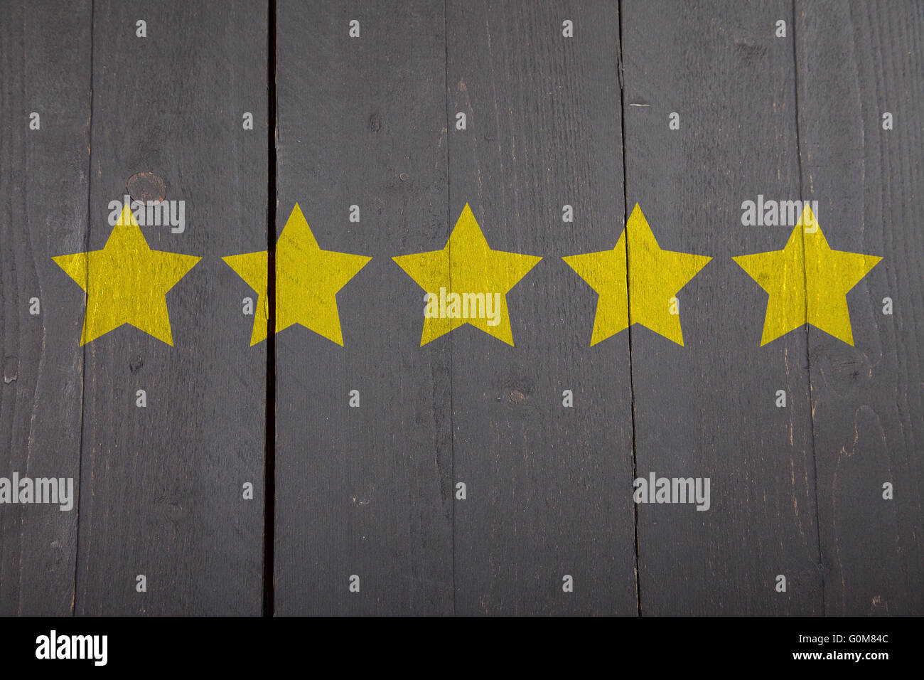 5 gelbe Ranking-Sterne auf schwarzem Hintergrund aus Holz Stockfoto