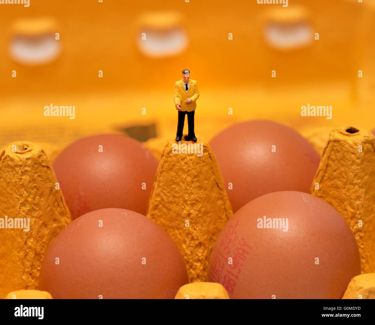 Ein Miniatur Figur Mann in einem gelben Jacke steht über 4 Eiern in einem Eierkarton Stockfoto