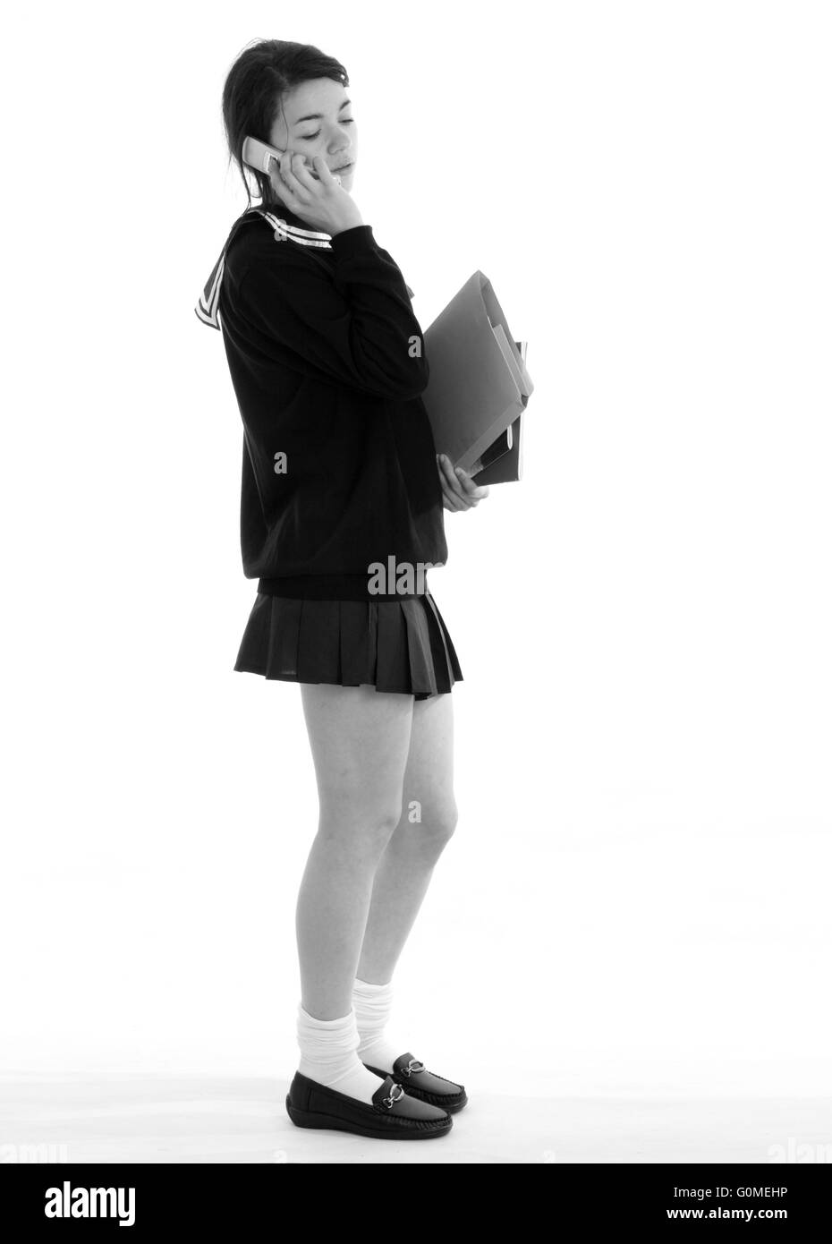 Mischlinge junge Frau in ein japanisches Schulmädchen Uniform gekleidet, mit einem sehr kurzen Rock tragen Bücher Stockfoto