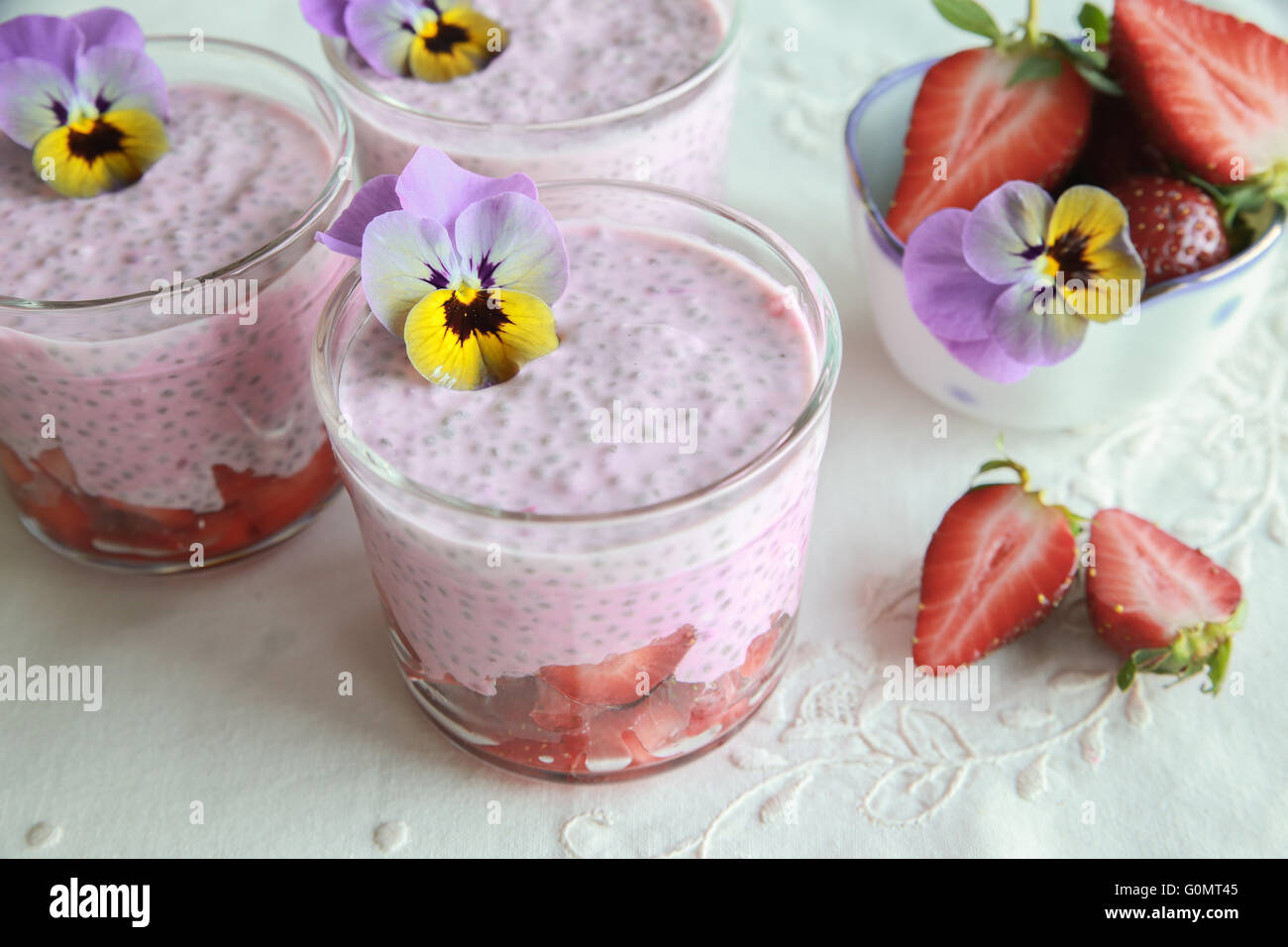 Hausgemachte rosa Chia Pudding mit Erdbeeren und essbaren Blüten Stockfoto