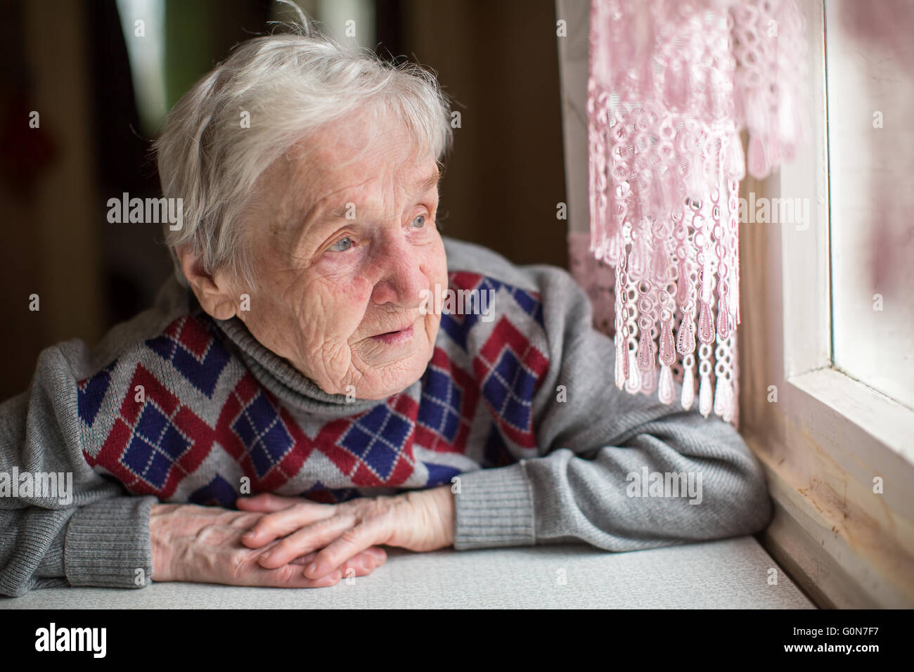 Eine ältere Frau sitzt und schaut aus dem Fenster. Stockfoto