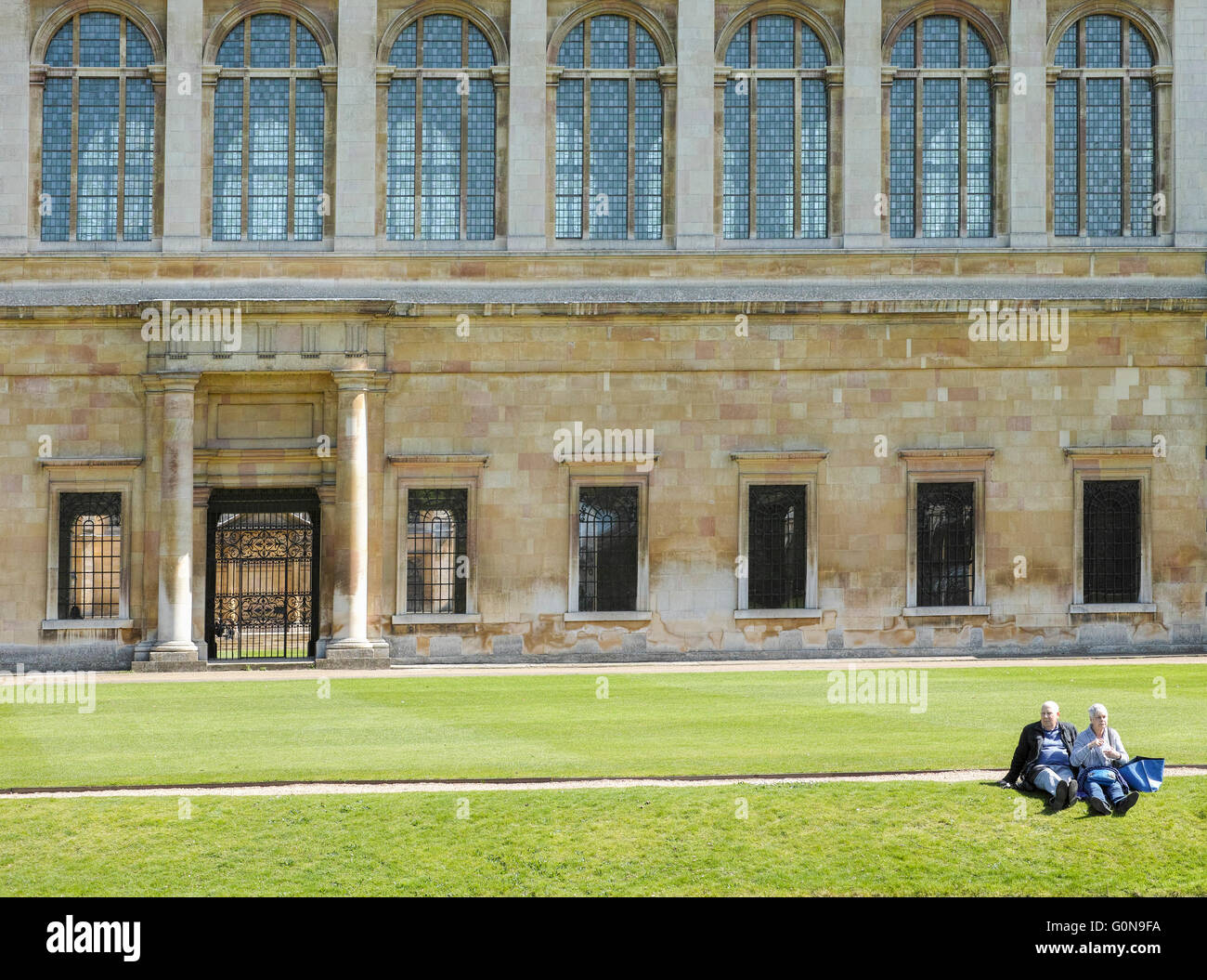 Älteres Ehepaar sitzen auf dem Rasen außerhalb der Wren Library am Trinity College der Universität Cambridge, England. Stockfoto