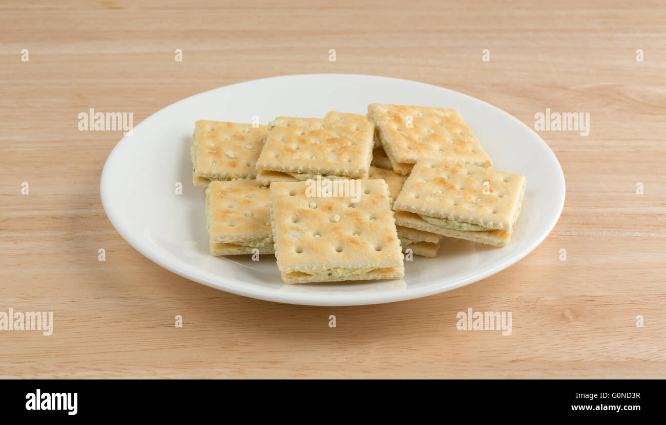 Seitenansicht der Frischkäse und Schnittlauch Cracker auf einem weißen Teller oben auf einer hölzernen Tischplatte. Stockfoto