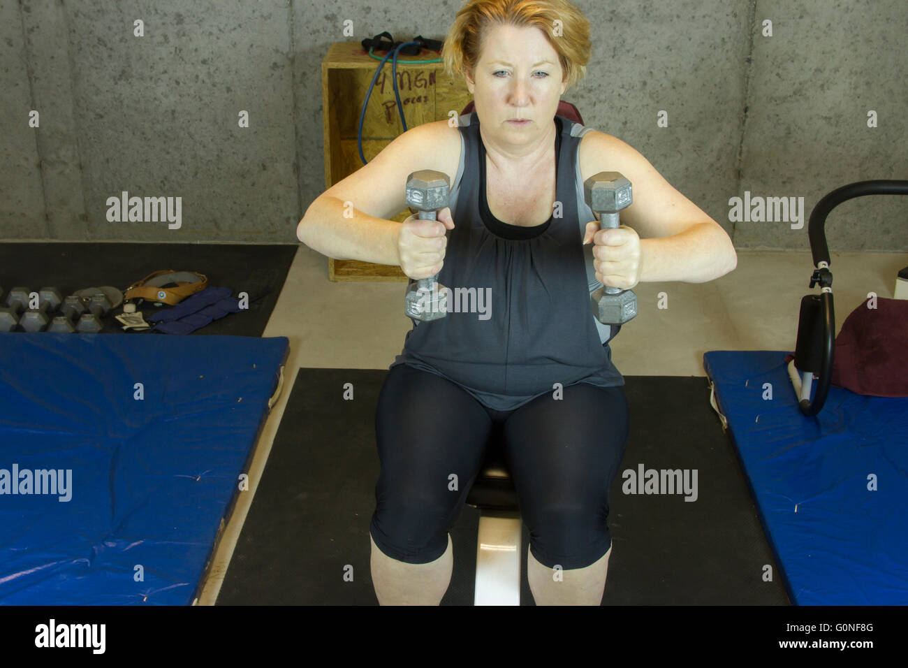 Reife Frau im Keller Fitnessraum mit Gewichten an Armen. Stockfoto