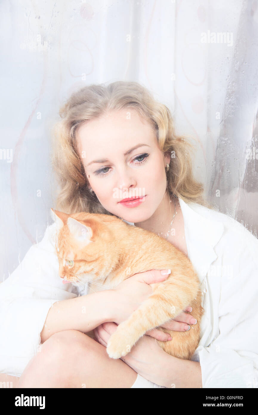 Schöne Frau am Fenster mit einer roten Katze an ihren Händen Stockfoto