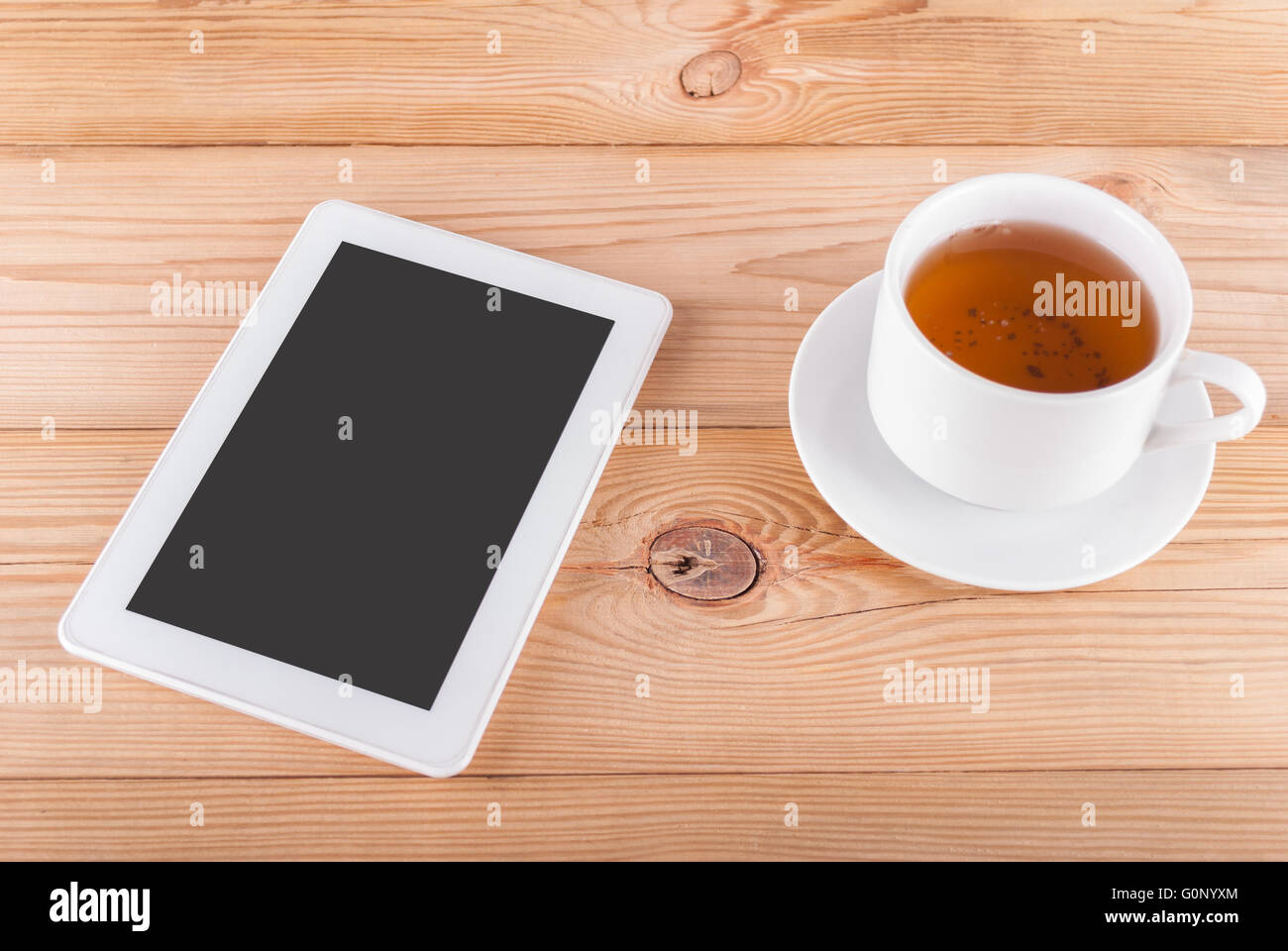 Tablet-Computer und eine Tasse Tee auf einem Holztisch. Stockfoto