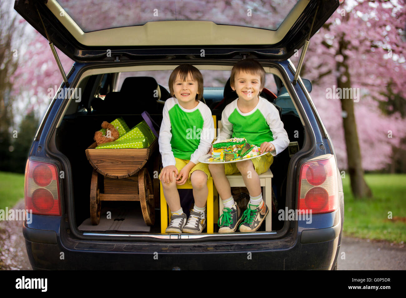 Nette Kinder, junge Brüder, sitzen im Kofferraum eines Autos, halten die Reste einer Geburtstagstorte trolley mit Geschenken im Auto, s Stockfoto