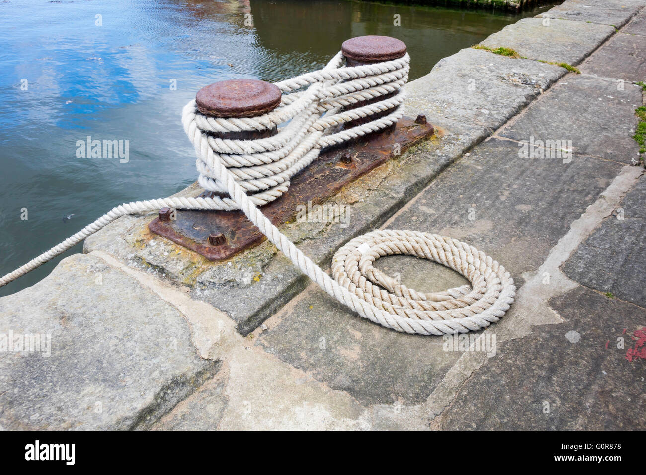 Festmacher Bitt Bitts oder Stollen auf Stein Steg Schneide fein säuberlich aufgerollt Liegeplatz Seil befestigt Stockfoto